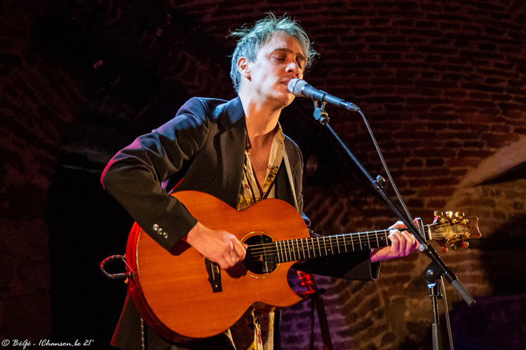 ET AVANT CELA Le premier concert de la soirée était assuré par Ivan Tirtiaux, dont NosEnchanteurs vous a déjà vanté les mérites à plusieurs reprises. Il était entouré de Mathieu Verkaeren à la contrebasse et à la grosse caisse, et de Raphaël Dumas à la mandoline et guitare 12 cordes. Un trio bien rôdé qui nous a délivré un set envoûtant, débutant par un long instrumental (parce que le chanteur n’a pas encore trouvé les paroles à y coller !), composé de morceaux extraits principalement du deuxième opus du chanteur (L’Oasis), et agrémenté d’un inédit tout neuf consacré à Julien Assange. Le répertoire d’Ivan Tirtiaux donne dans le folk-blues à tendance contemplative. Un concert qui en aura déconcerté quelques-uns, rétifs à se laisser entraîner dans cet univers qui prend son temps. Mais ceux qui s’y sont abandonnés se sont régalés.